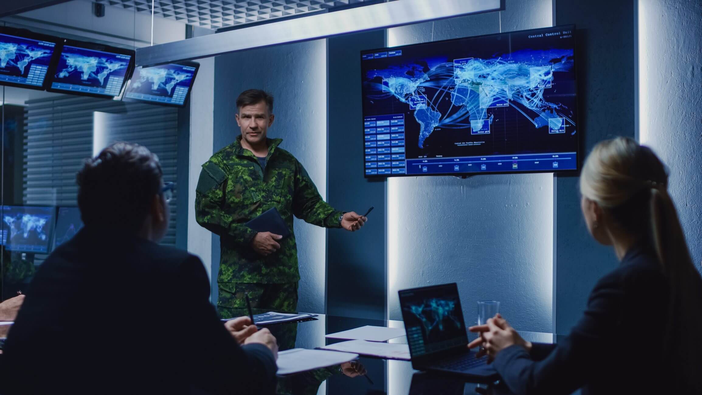 Military briefing with global map on screen.