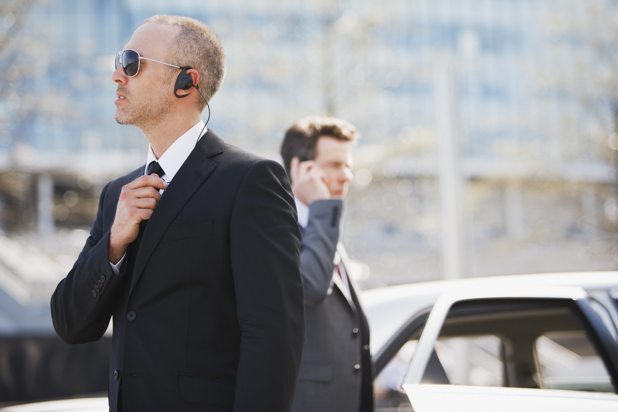 Security personnel with earpieces near car.
